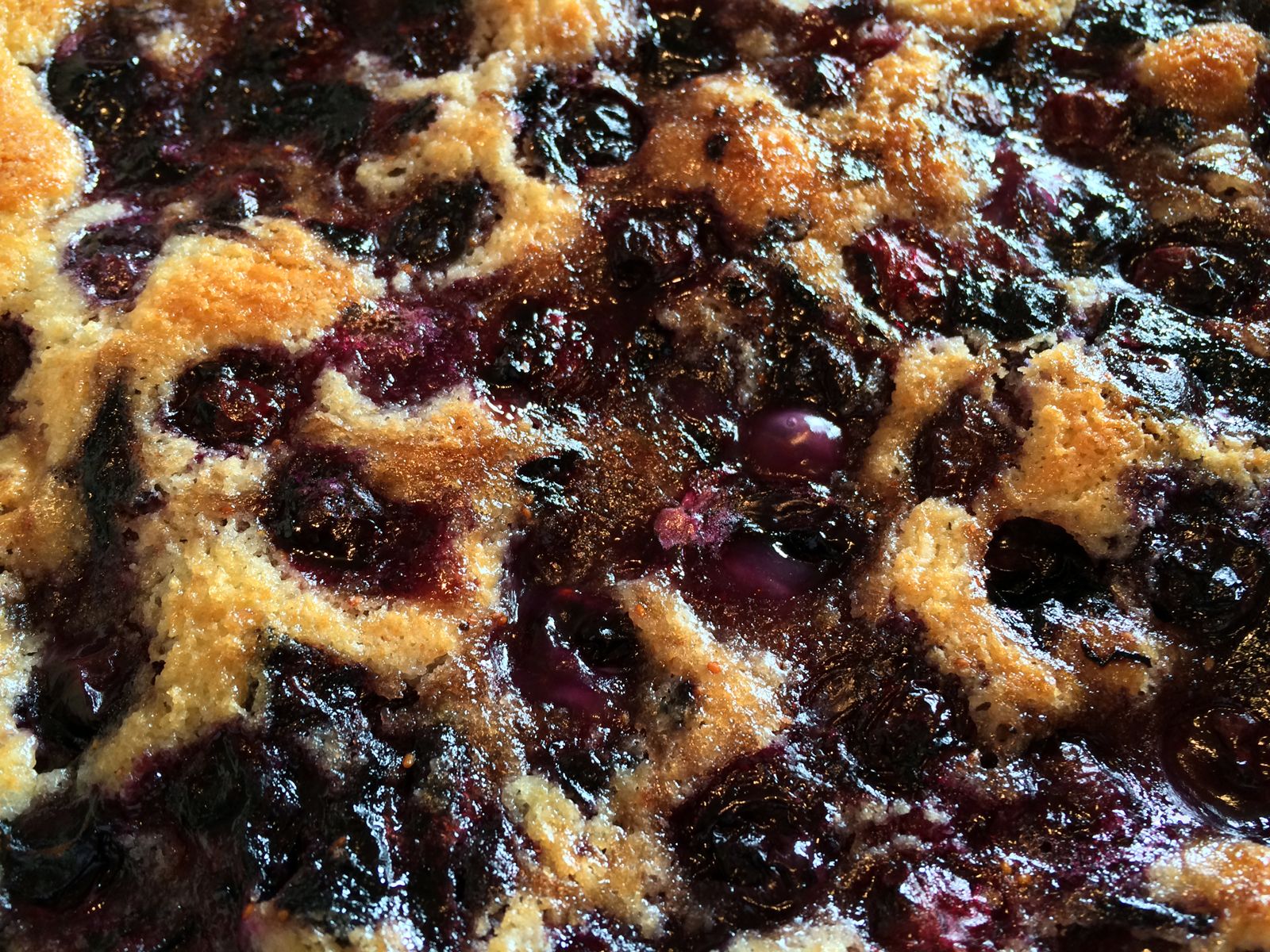 Golden-brown berry cobbler cake with a crispy sugar topping, bubbling with vibrant blueberries and raspberries.